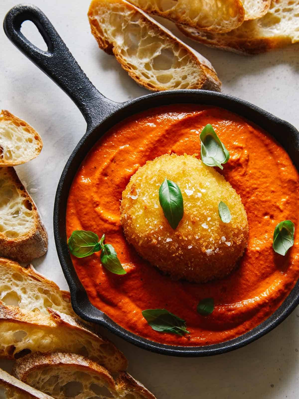 Fried burrata over romesco sauce in a skillet with bread.