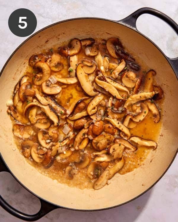 Mushrooms with stock cooking down in a skillet.