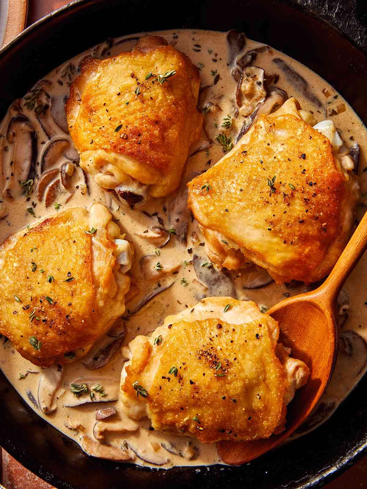 Crispy chicken thighs in a skillet with a creamy mushroom sauce.