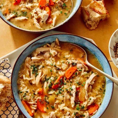 Chicken and rice soup in two bowls with bread on the side.